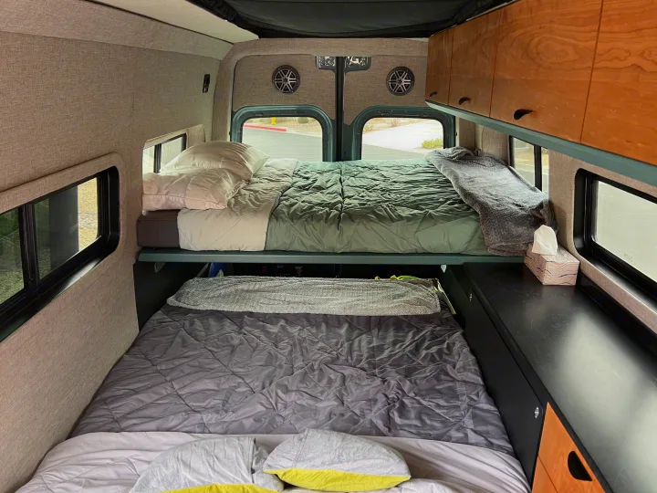 Stacked bunk beds inside an RV rental, featuring custom cabinetry and large windows for scenic views.. Off Highway Van Off Highway Van Class B 2024