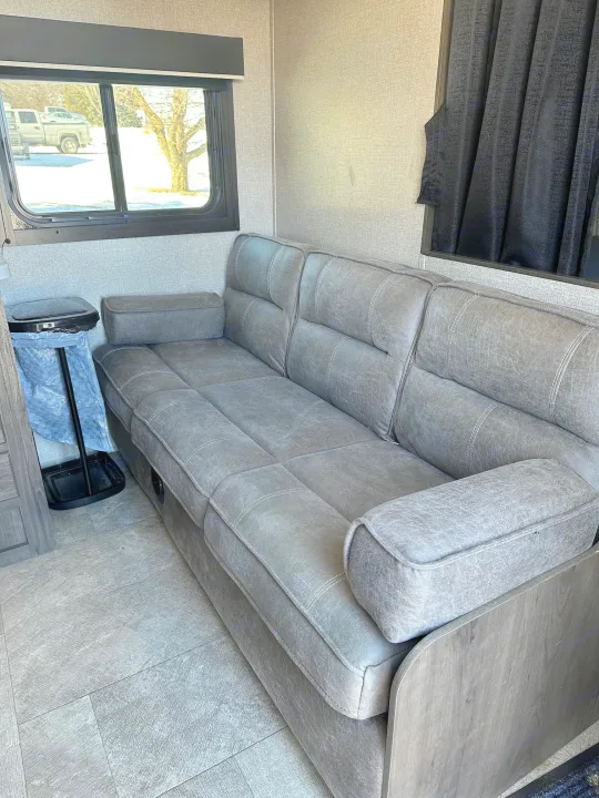 Modern RV rental: a spacious interior with a long, comfy gray sofa & a beautiful snowy winter view from the window.. Jayco Jay Flight SLX 2020