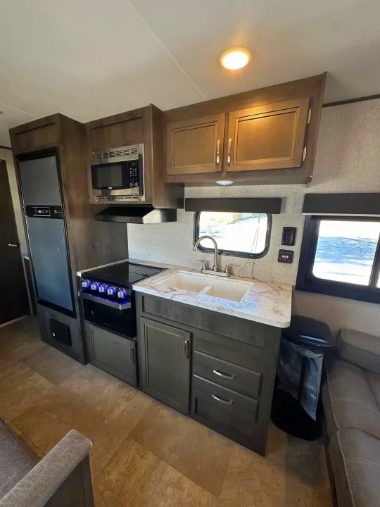 Interior of an RV rental showing a modern, compact kitchen with fridge, microwave, stove, and sink.. Jayco Jay Flight SLX 2020