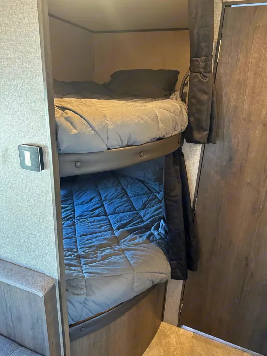 Inside an RV rental: two cozy bunk beds with bedding, featuring a Dometic control panel and privacy curtain for comfort.. Jayco Jay Flight SLX 2020