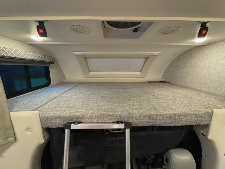 Inside an RV rental, the spacious overhead bunk bed offers a comfortable sleeping area with a skylight, side window, and ceiling fan.. Thor Quantum 2022