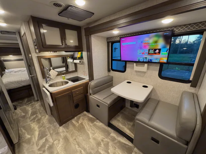 RV rental interior featuring a compact kitchen, dinette with TV, and a glimpse into the comfortable bedroom.. Thor Quantum 2022