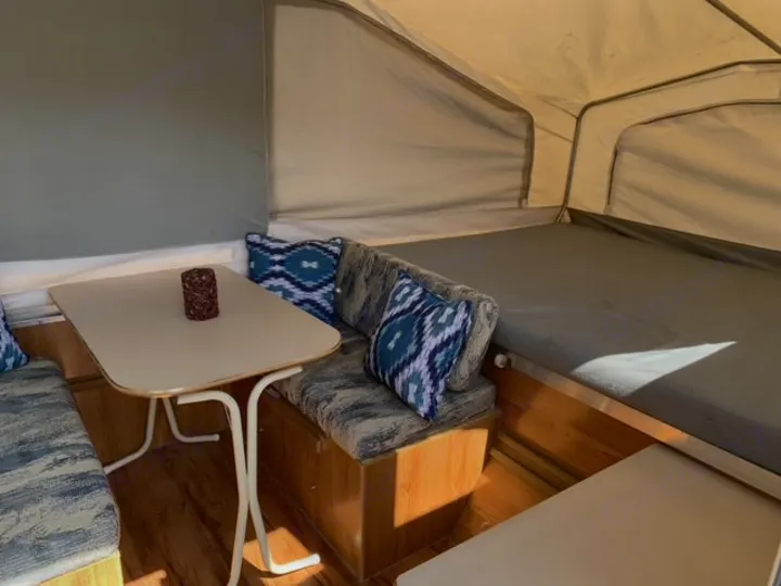Inside an RV rental: Cozy pop-up camper featuring a dining area with bench seating, a table, and a comfortable bed.. Palomino Pinto 1999