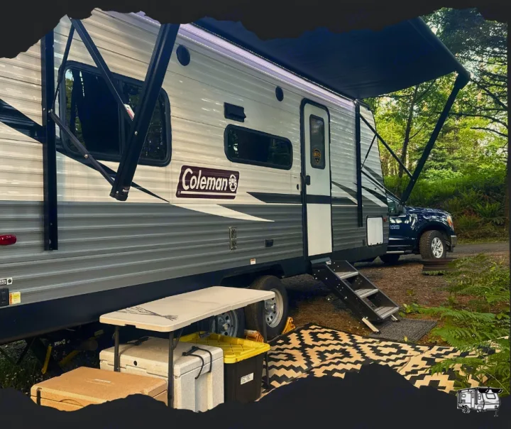 An RV rental at a forest campsite, featuring an extended awning, outdoor mat, table, and steps for outdoor living.. Dutchmen Coleman Lantern LT 2021
