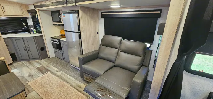 Inside this modern rv rental: a full kitchen with microwave, fridge, and stove, next to a comfy reclining sofa.. Heartland RVs Sundance Ultra Lite 2022
