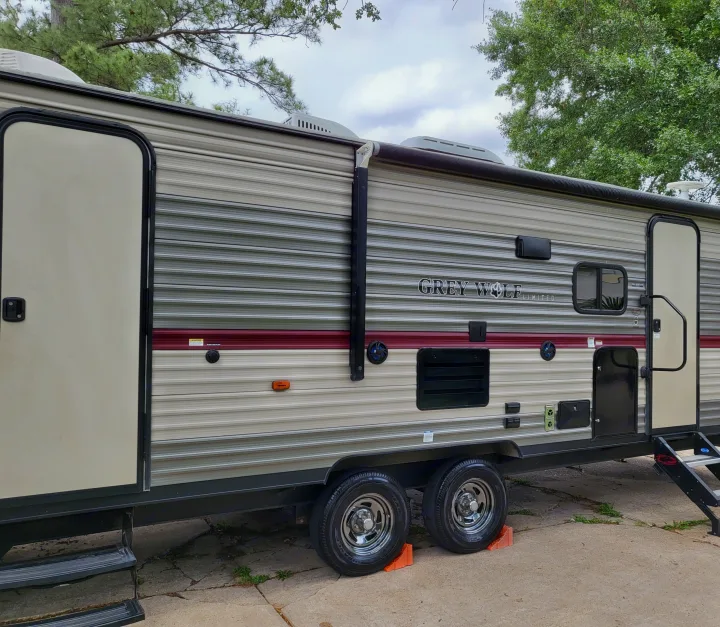 A Grey Wolf travel trailer, supported by orange chocks, is parked outdoors. Ideal for your next RV rental or camping trip.. Forest River Cherokee Grey Wolf 2018