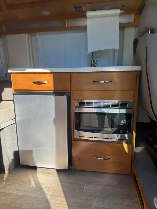 RV rental kitchen: light wood cabinets, white countertop, sink, microwave, and refrigerator.. Coachmen Nova 2021
