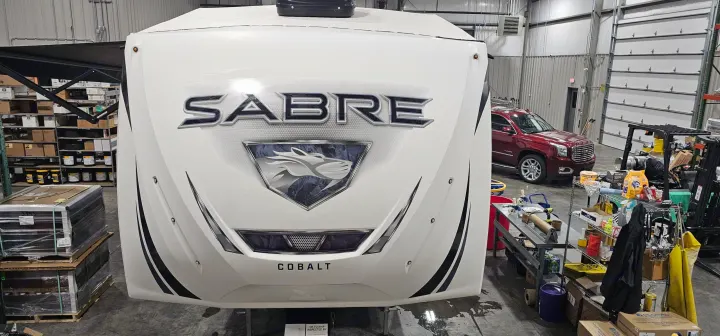 Sleek white Sabre Cobalt travel trailer in a warehouse, likely awaiting an RV rental or delivery. Visible branding & horse logo.. Forest River Sabre 2019