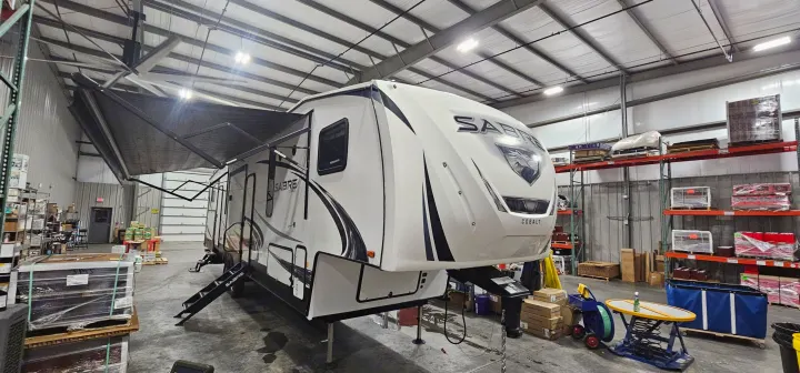 A large white Sabre Cobalt fifth-wheel RV, with awnings extended, inside a well-lit warehouse; perfect for rv rental.. Forest River Sabre 2019