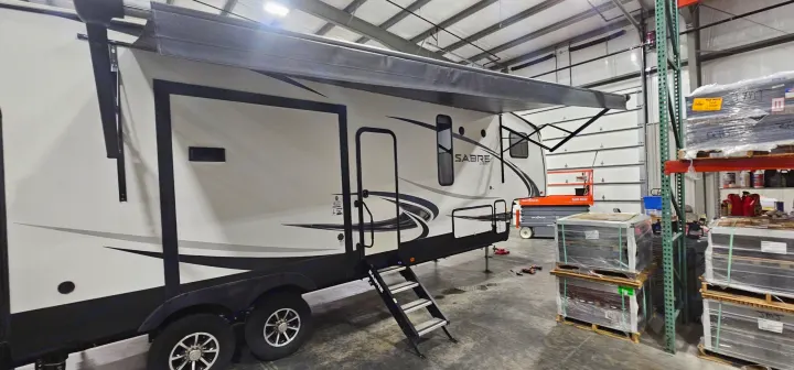 Sabre Cobalt travel trailer RV rental with awning extended, parked indoors for service or storage in a warehouse setting.. Forest River Sabre 2019