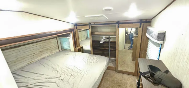 Modern RV rental bedroom with a large bed, textured headboard, and mirrored barn-door closet for storage.. Forest River Sabre 2019