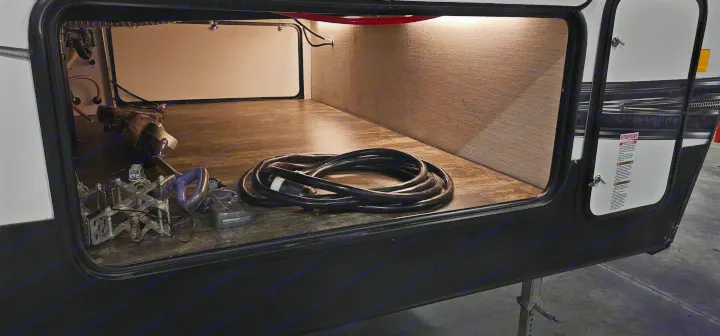 This rv rental's pass-through storage is well-lit, holding a coiled shore power cord, Dyson vacuum, and battery charger.. Forest River Sabre 2019