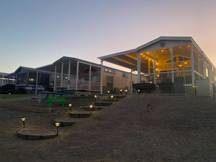 Evening view of cozy park model RV rentals with illuminated porches and pathway lights, perfect for a relaxing stay.. ATHMS CCHPT 2019