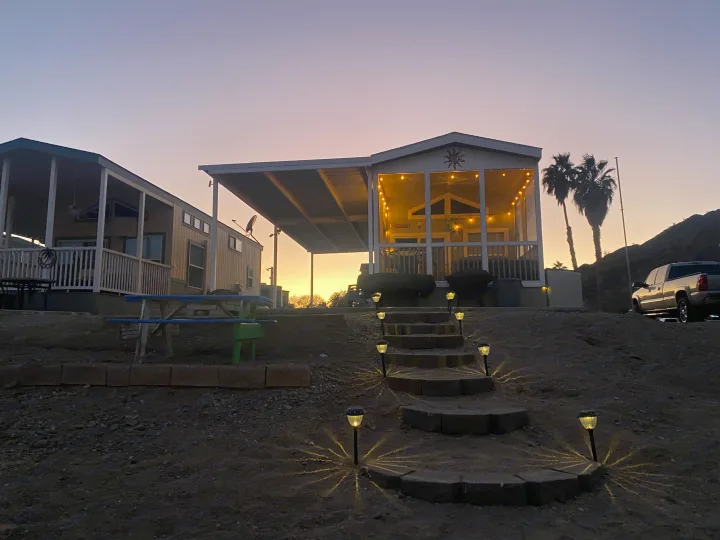 Cozy RV rental: A manufactured home with a lit porch & solar-lit steps, illuminated at sunset for a desert getaway.. ATHMS CCHPT 2019