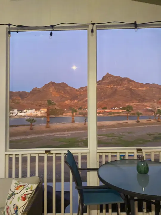 Scenic dusk from an RV rental, featuring a bright moon over a lake, mountains, and palm trees. Cozy porch setting.. ATHMS CCHPT 2019