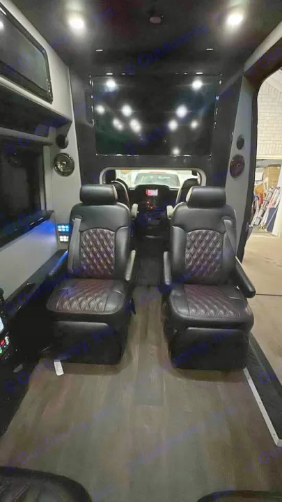 RV rental interior featuring two black leather captain's chairs with diamond stitching, wood flooring, and ceiling-mounted screens.. Midwest Automotive Designs Midwest Automotive Designs Class B 2016