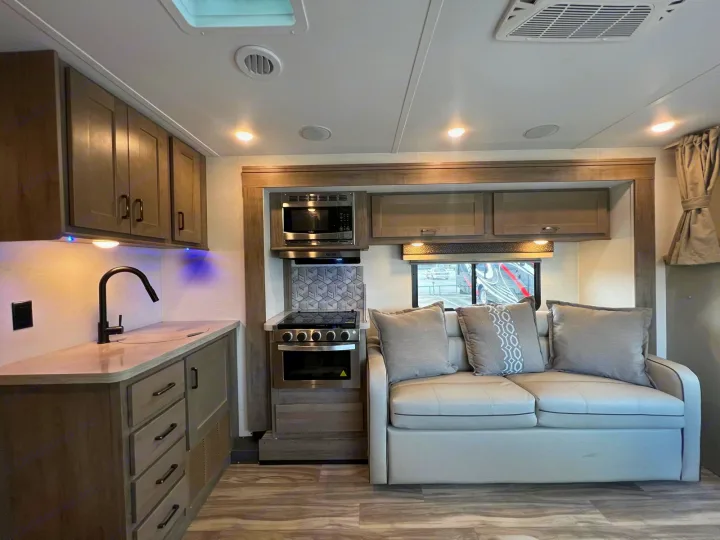 This RV rental features a well-equipped kitchen with a microwave, stove, and sink, alongside a comfortable sofa for relaxation.. Gulf Stream Conquest 2025