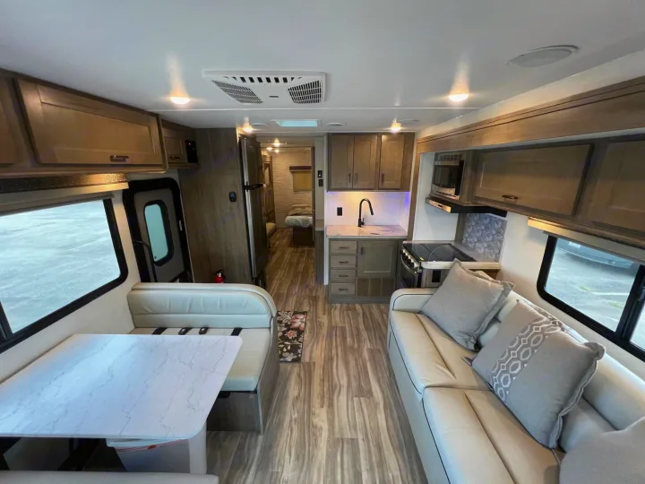 Modern RV rental interior with kitchen, dinette, and sofa living area. Features light wood cabinets, flooring, and bright lighting.. Gulf Stream Conquest 2025