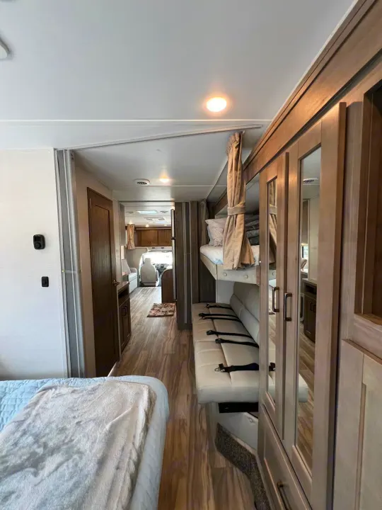 Spacious rv rental interior showing bunk beds, a sofa, modern decor, and a hallway leading to the front cab.. Gulf Stream Conquest 2025