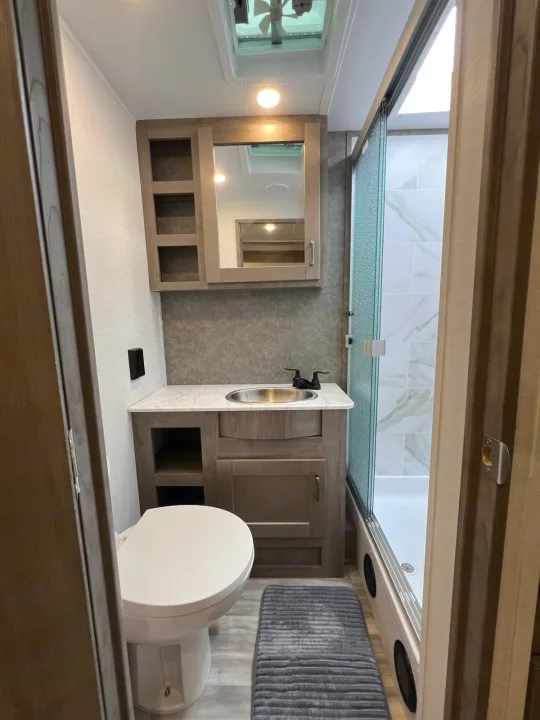 This clean, modern RV rental bathroom features a compact toilet, vanity with sink, medicine cabinet, and glass-enclosed shower.. Gulf Stream Conquest 2025