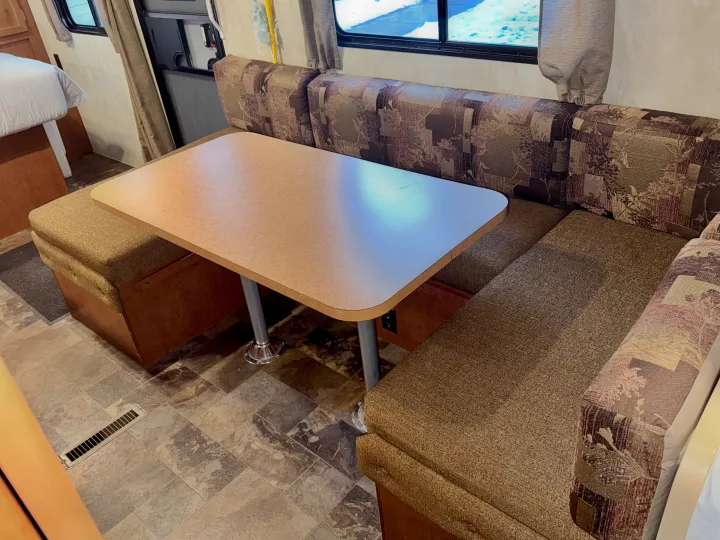 Cozy RV rental dinette with patterned bench seating, a light-colored table, and visible bed area.. Nash Nash Trailer 2016