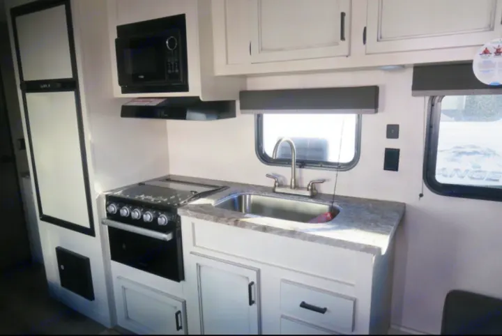 Inside an RV rental: a modern kitchen with fridge, microwave, oven, sink & ample cabinets, great for road trips.. Open Range Open Range 2021