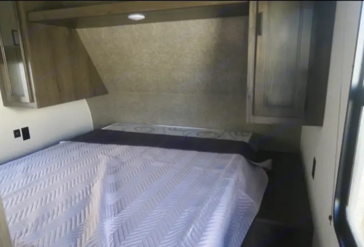 RV rental bedroom showing a white quilted bed, light wood overhead cabinets, and wall outlets.. Open Range Open Range 2021