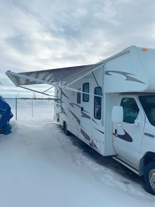 White RV rental with brown graphics and an extended awning in snowy winter storage.. Forest River Sunseeker 2008