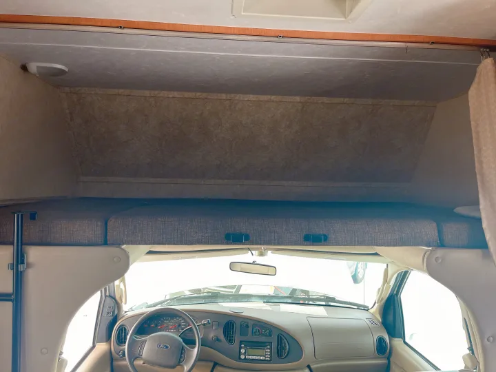 Inside an RV rental: a cozy cab-over bed overlooks the driver's cockpit/dashboard, perfect for road trips in a motorhome.. Forest River Sunseeker 2008