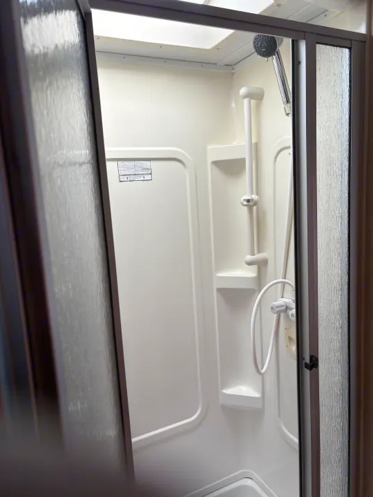Compact RV rental shower interior with white molded walls, showerhead, and textured glass door.. Forest River Sunseeker 2008