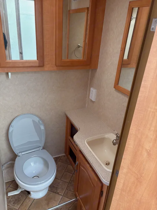 Compact rv rental bathroom featuring a white toilet, light-colored sink with counter, wooden overhead cabinets, and wall-mounted mirrors.. Forest River Sunseeker 2008