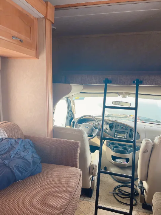 RV rental interior view: driver's area with steering wheel, ladder for overhead bunk, and brown fabric seating.. Forest River Sunseeker 2008