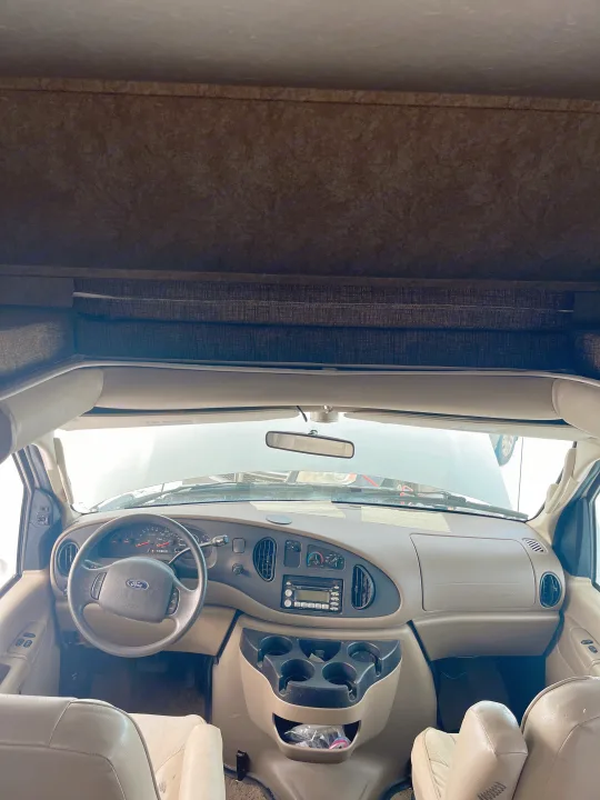 RV rental cockpit: features a Ford steering wheel, dashboard controls, and an over-cab bed visible above.. Forest River Sunseeker 2008