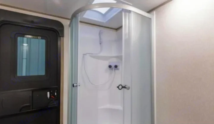 RV rental interior features a compact, curved glass shower cabin with skylight and a dark entry door. Efficient use of space.. Forest River Cherokee Alpha Wolf 2021