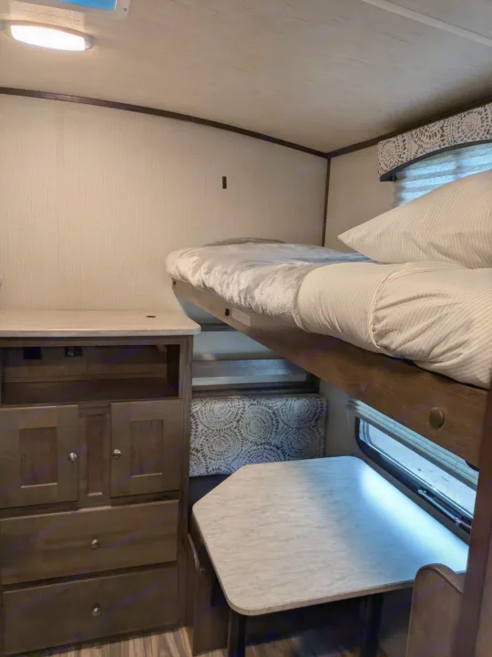 Compact RV rental interior with bunk beds, a dresser, and a dinette area featuring a small table.. Cruiser RV MPG Ultra Lite 2019