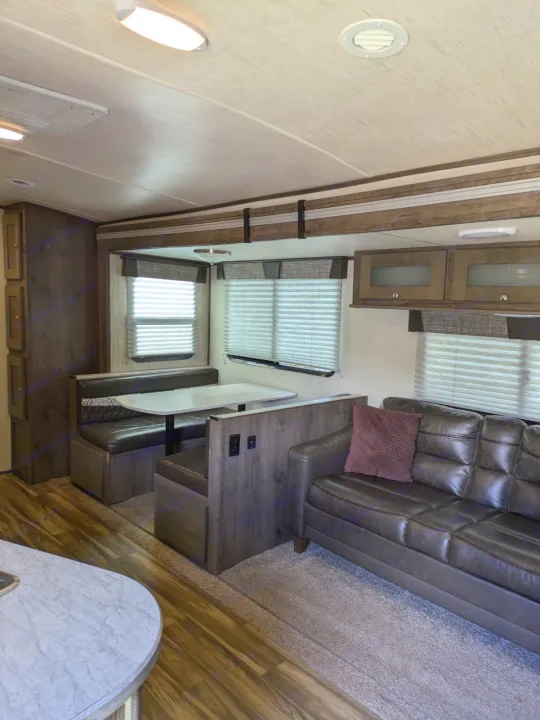 Cozy RV rental interior: dinette, brown leather sofa, wood-look floor, and overhead storage.. Cruiser RV MPG Ultra Lite 2019