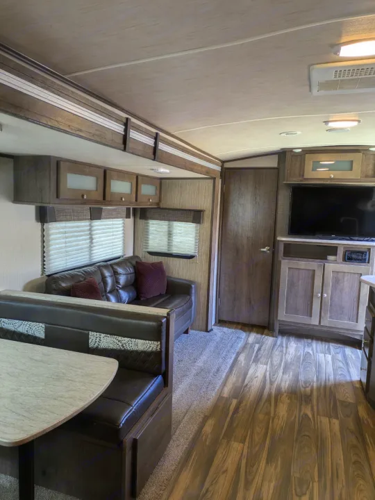 Modern RV rental living space with a brown sofa, dinette booth, overhead cabinets, and entertainment center.. Cruiser RV MPG Ultra Lite 2019