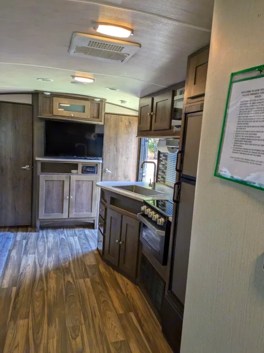 Inside a modern RV rental, featuring a kitchen with sink and stove, living area with TV, and wood-patterned floor.. Cruiser RV MPG Ultra Lite 2019