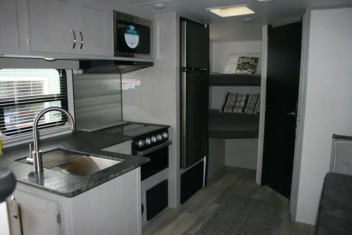 This RV rental showcases a functional kitchen with a sink, oven, and microwave, alongside built-in bunk beds.. Forest River Tracer 2022