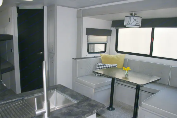 Modern RV rental interior: grey dinette, dark kitchen counter/sink, and bright windows. A cozy space for your next adventure.. Forest River Tracer 2022