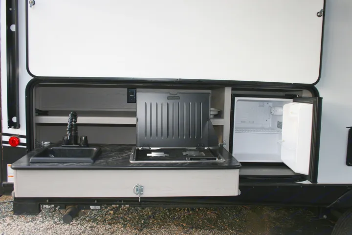 RV rental with an open compartment revealing an outdoor kitchen: sink, two-burner stove, and small refrigerator.. Forest River Tracer 2022