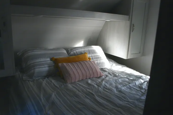 Bright RV rental bedroom: striped bed, two large, one yellow, and one pink pillow. Light wood interior.. Forest River Tracer 2022