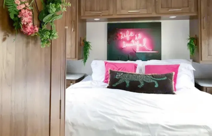 Cozy RV rental bedroom with white bedding, pink pillows, and a 'Life is beautiful' neon sign for a stylish travel retreat.. Coachmen Pursuit 2021