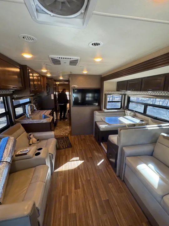 Spacious rv rental interior featuring a full kitchen, comfortable living area with TV, and dinette seating on wood floors.. Thor A.C.E. 2019