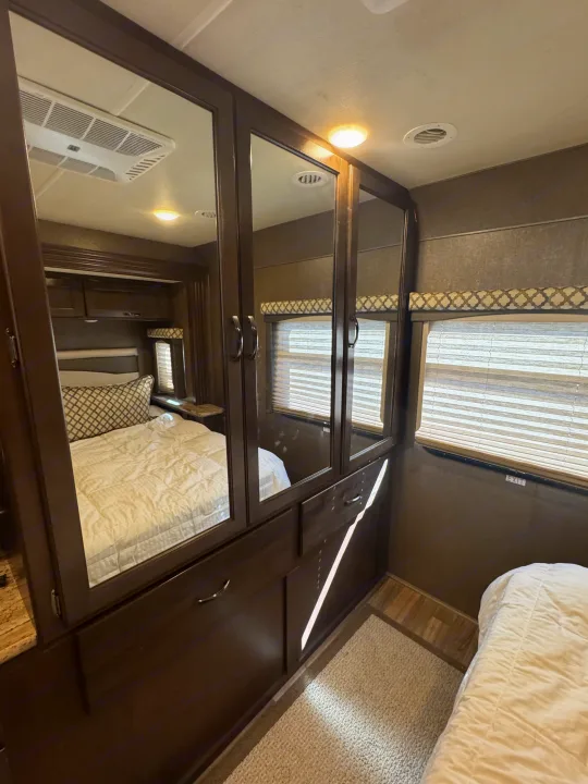 RV rental bedroom featuring a mirrored wardrobe, comfortable bed, overhead AC, and window. Compact & functional space.. Thor A.C.E. 2019