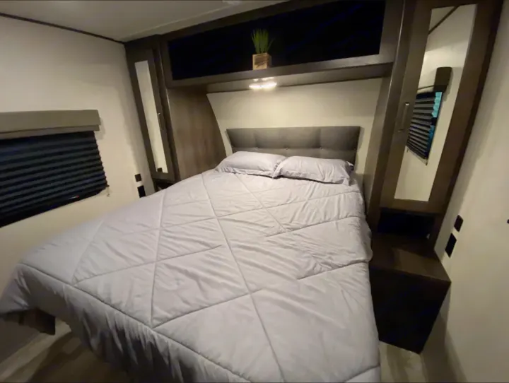 RV rental bedroom featuring a comfortable queen bed, overhead storage, reading lights, and mirrored closet.. Grand Design Transcend Xplor 2022