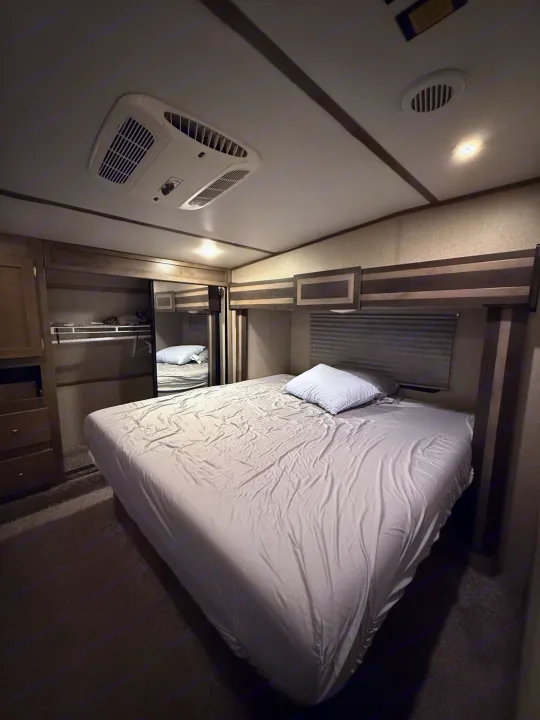 Cozy RV rental sleeping area with a bed, wardrobe, and overhead AC unit for comfortable travel nights.. Keystone Sprinter 2018