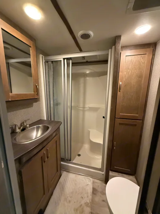 Inside an RV rental bathroom, featuring a compact shower, vanity with sink, mirror, storage cabinets, and toilet.. Keystone Sprinter 2018