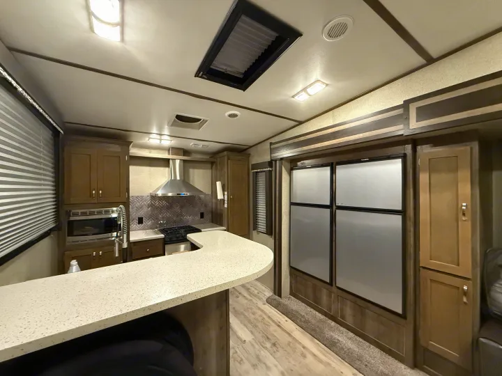 Modern RV rental interior: well-equipped kitchen with counter, microwave, stove, & large refrigerator. Bright lighting throughout.. Keystone Sprinter 2018