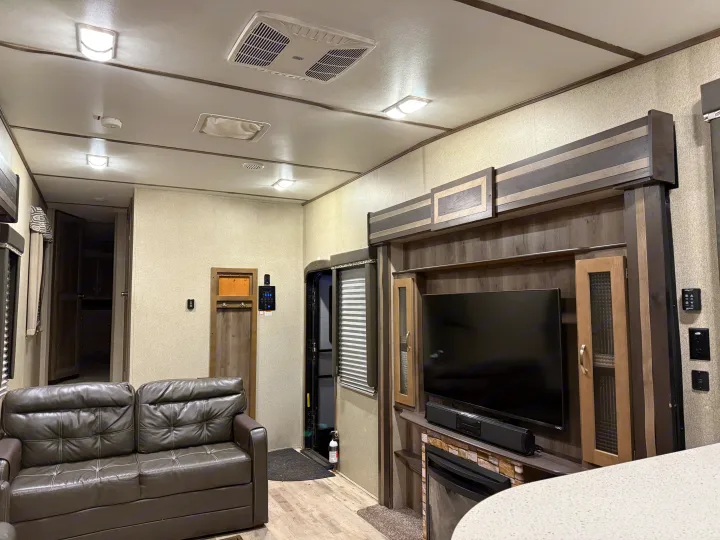 Bright RV rental living space with a comfortable leather sofa, TV, fireplace, and overhead AC unit for comfort.. Keystone Sprinter 2018